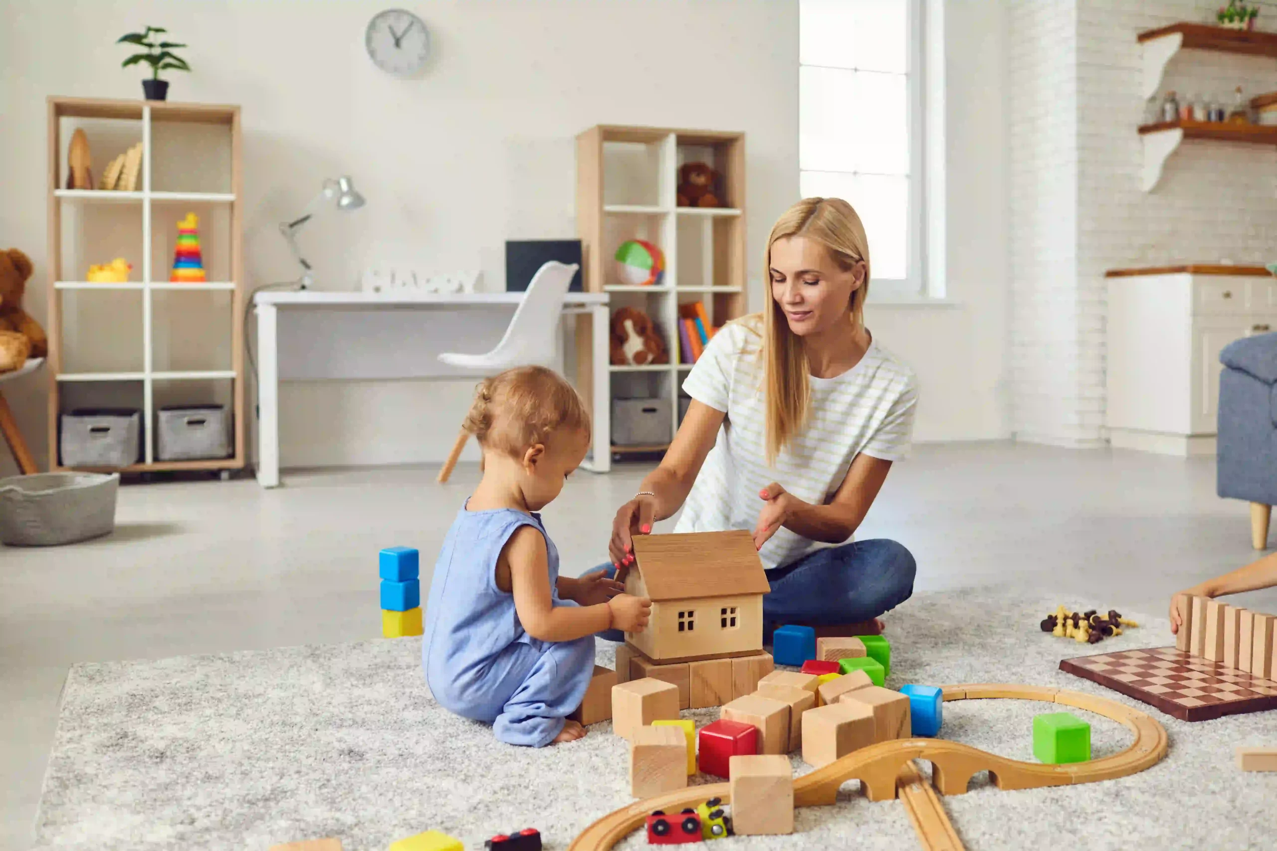Une professionnelle joue avec un jeune enfant et des cubes en bois dans un salon.
