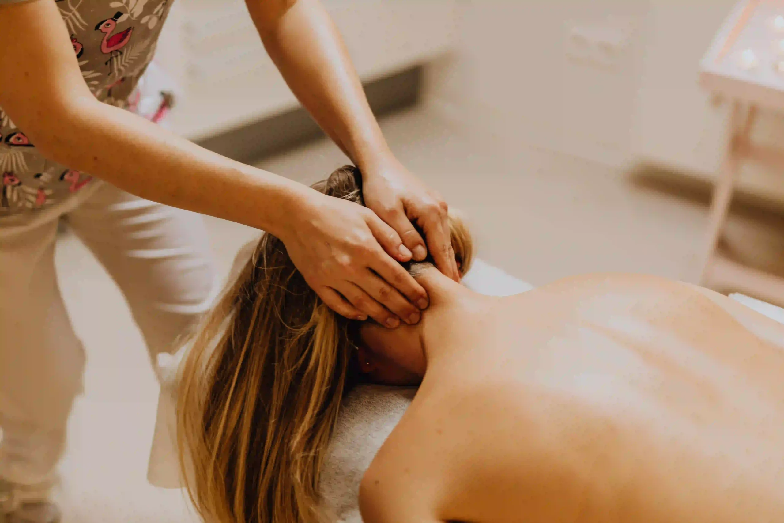 Une professionnelle masse la nuque d’une femme allongée sur une table de massage.