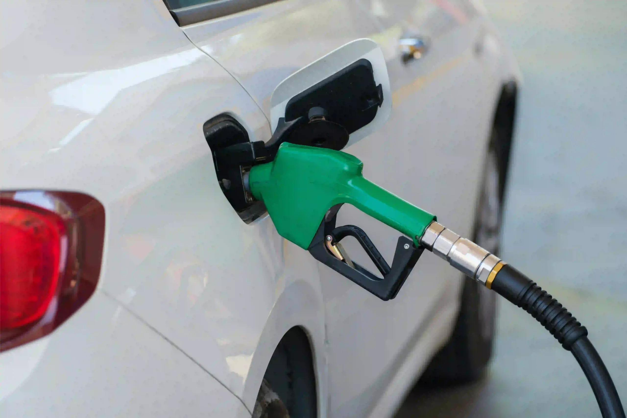 Une pompe à carburant verte est insérée dans le réservoir d’une voiture blanche.