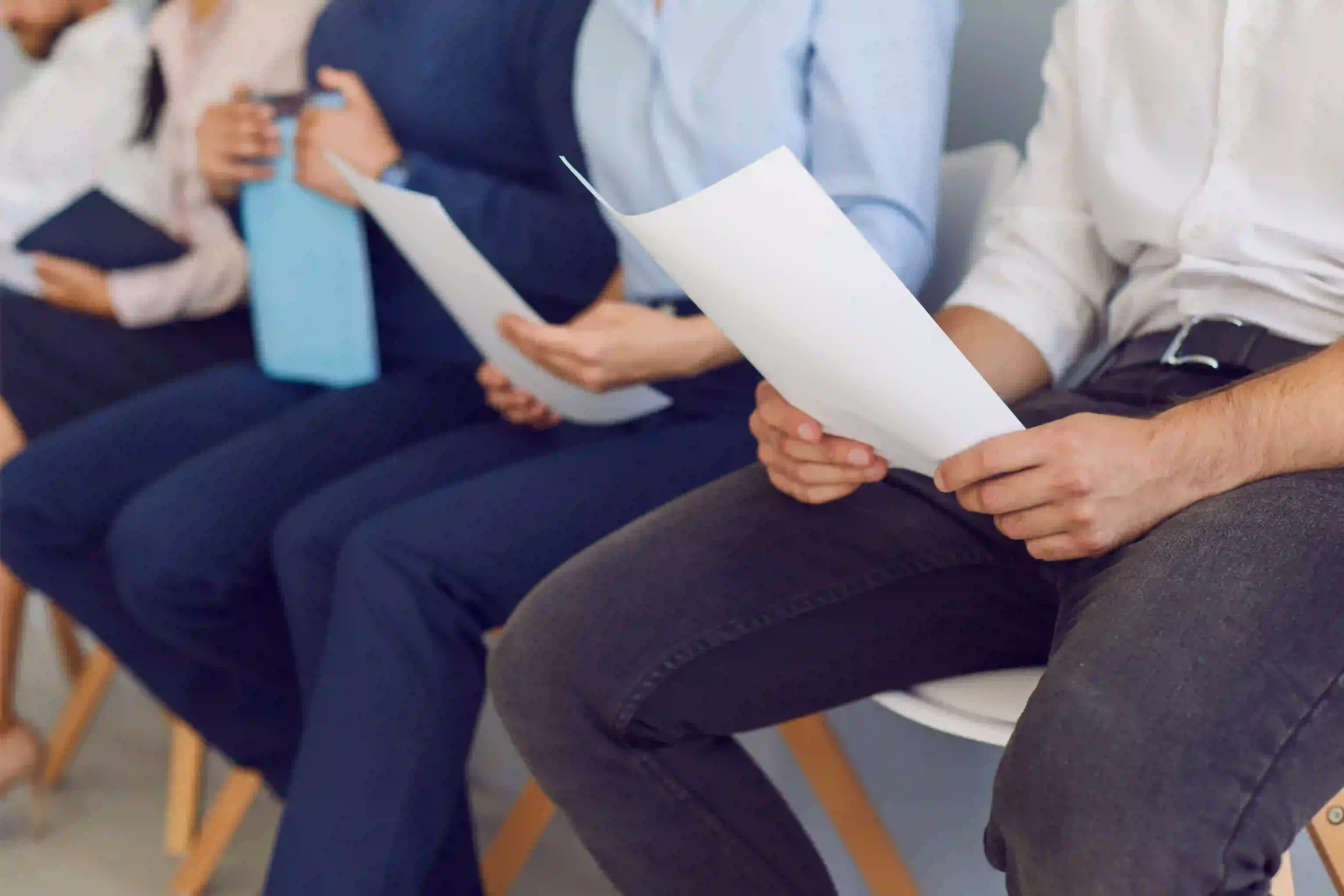 Plusieurs candidats assis dans une salle d’attente tiennent leur CV avant un entretien d’embauche.