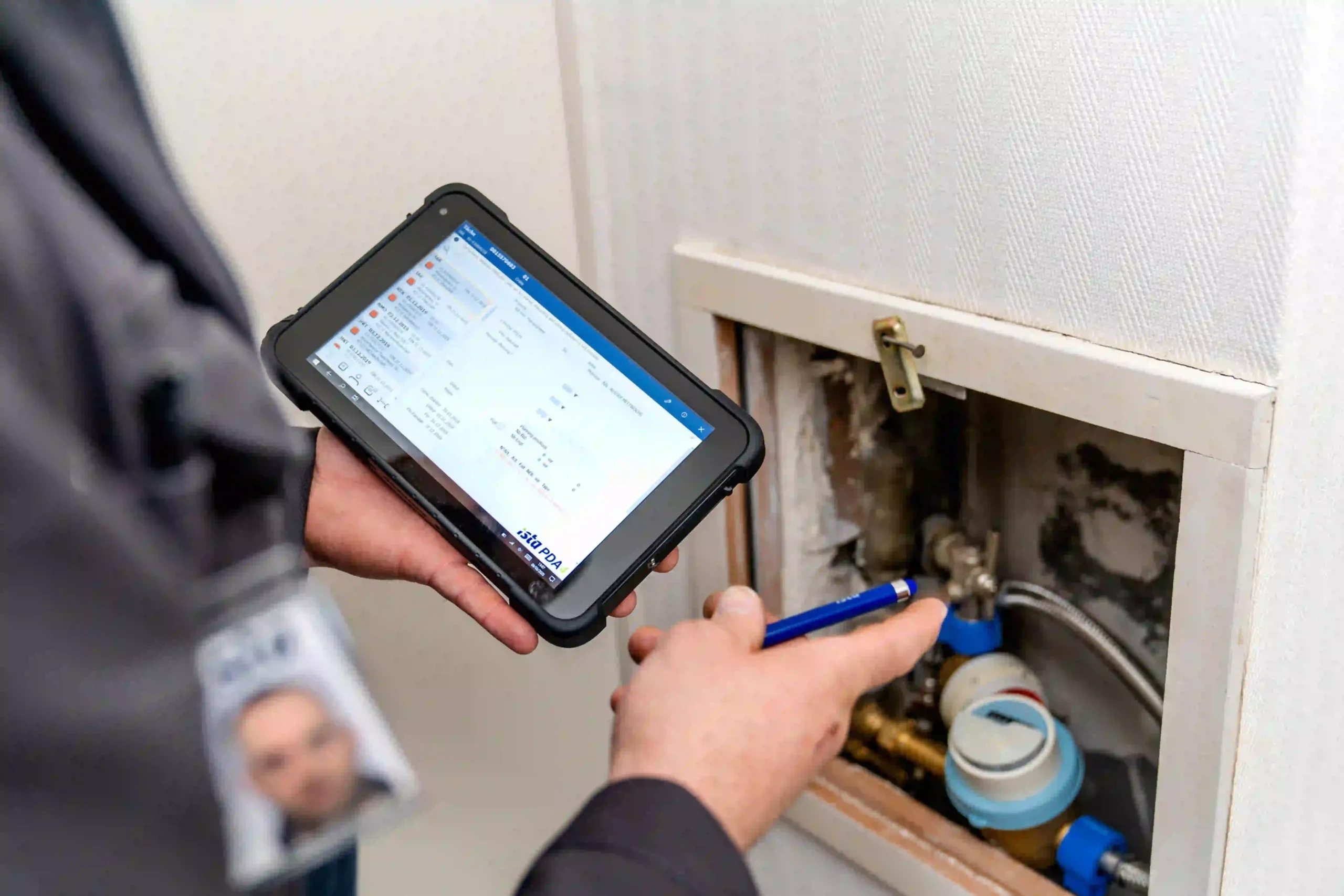 Un technicien ista consulte une tablette lors du contrôle d’un compteur d’eau installé dans un logement.