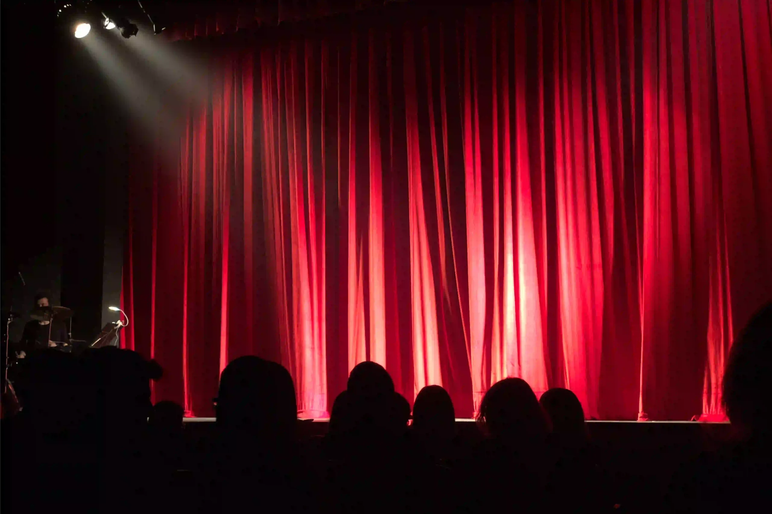 Un rideau de théâtre rouge fermé est éclairé par un projecteur devant le public.