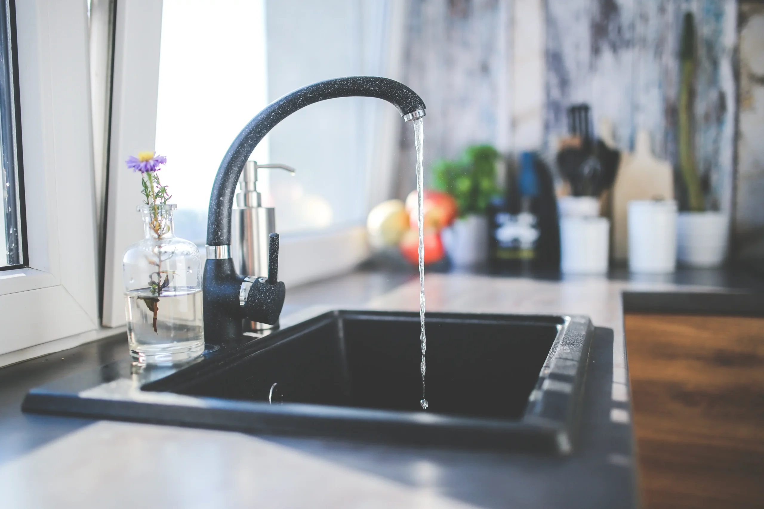 De l’eau coule d’un robinet noir dans l’évier d’une cuisine.