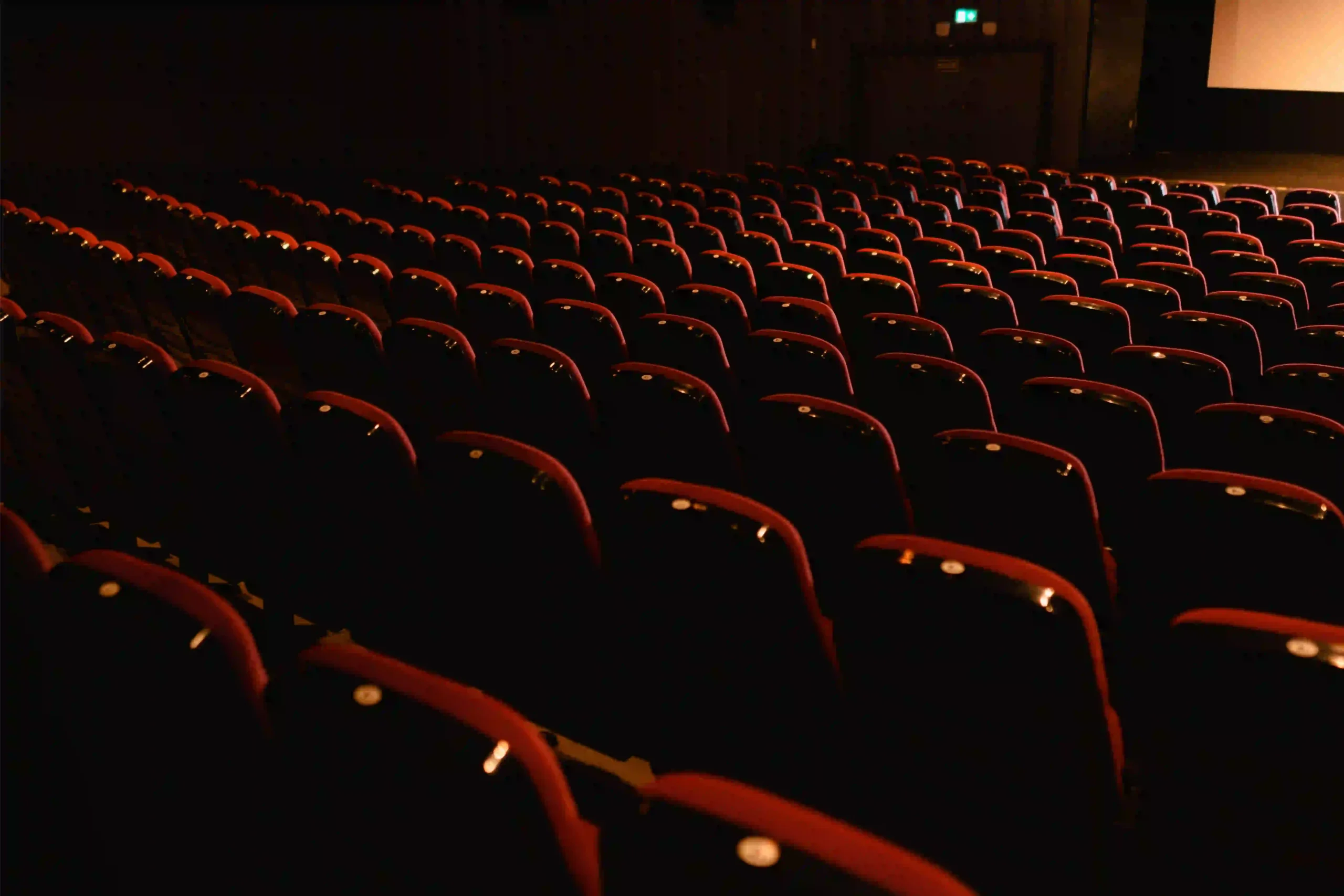 Une salle de théâtre vide composée de nombreuses rangées de fauteuils rouges face à la scène.