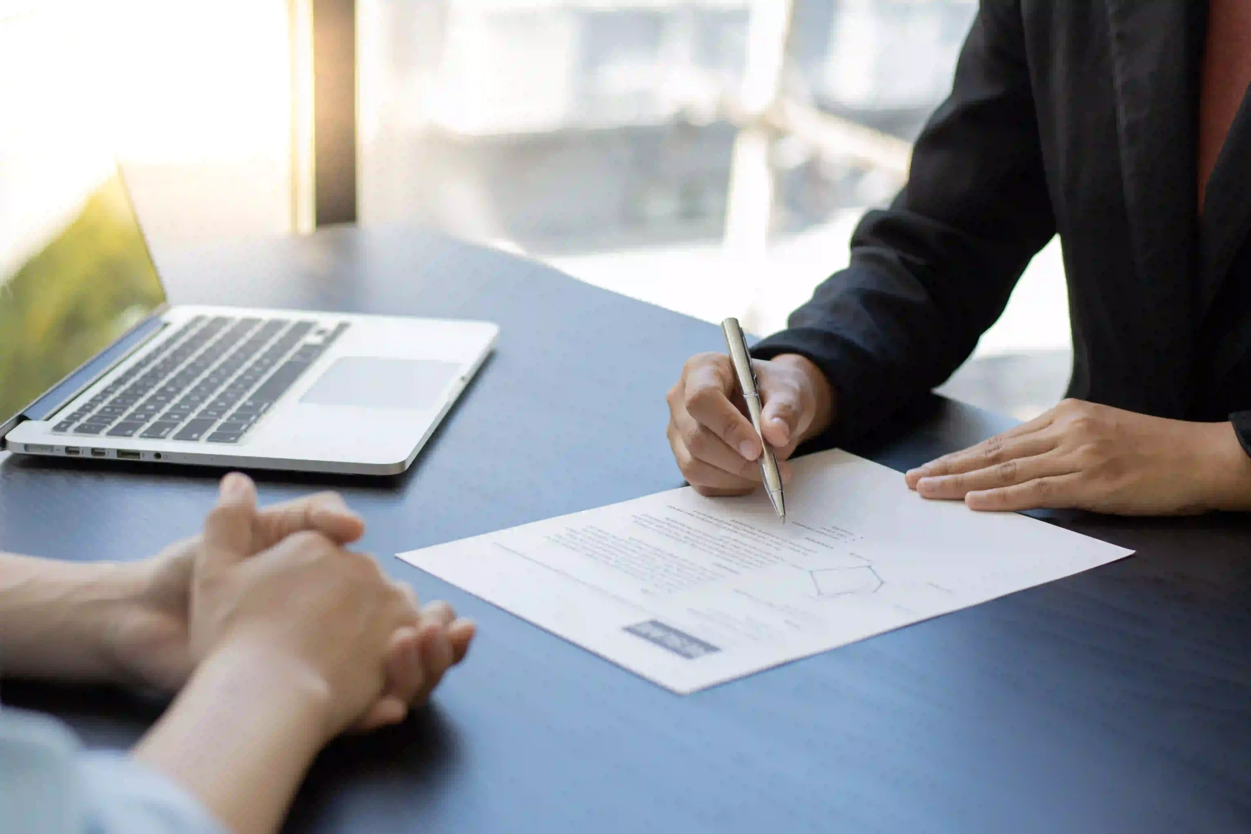 Une personne signe un contrat posé sur une table, face à un interlocuteur.