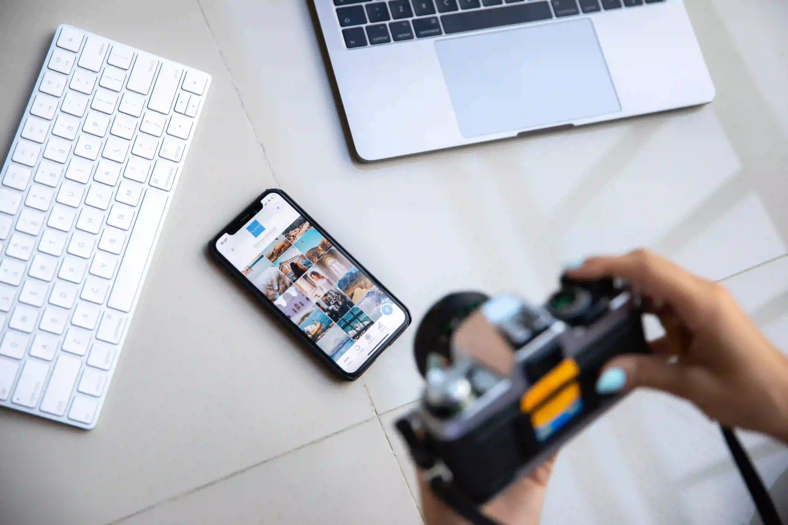 Une personne tient un appareil photo devant un smartphone affichant une galerie de publications sur les réseaux sociaux.