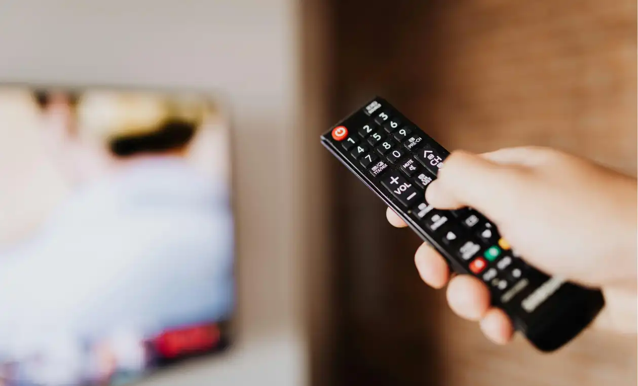 Main tenant une télécommande face à un téléviseur