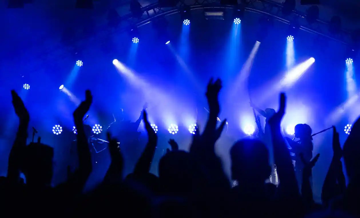 Public les bras levés devant une scène de concert éclairée en bleu